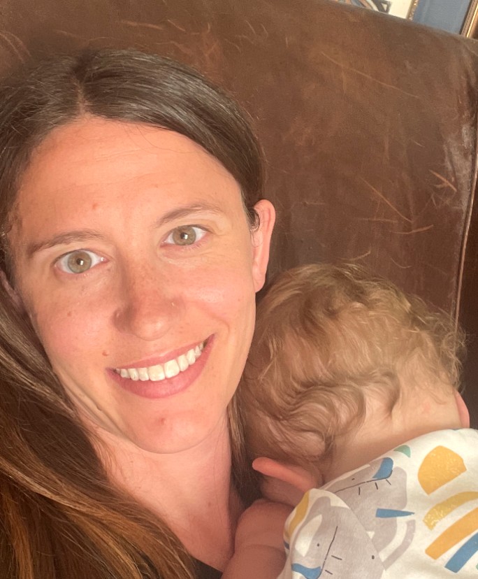 Kim smiling on a leather armchair with her toddler nestled into her shoulder